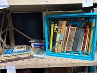 Wide view of the blue crate filled with vintage books on a shelf, showing the assortment and condition of the books.