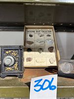Photo shows the black cast iron combination safe bank with gold detailing, the box labeled Souvenir Rock Collection containing 12 rock/mineral gemstones, and the lucite enclosed 1971 Liberty Head dollar coin paperweight alongside the rocks.