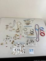 Top-down view of assorted rings, gold plated earrings, plastic bracelets, necklaces, and pendants laid out on a white surface.