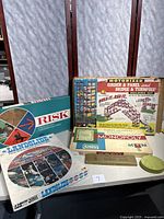 Photo showing all items together on a table: Kenners Motorized Building Set box, Risk, Landslide, Monopoly games, and cribbage board.
