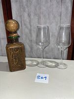 Full view of vintage leather wrapped decanter and two clear wine glasses on chair