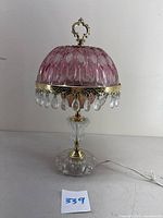 Front view of the vintage pink cranberry glass boudoir lamp with brass fittings and hanging crystal-like droplets, showing the full lamp including its clear cut glass base.