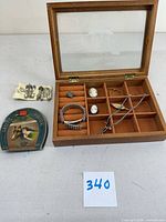 Open wooden jewelry box showing etched glass lid and various vintage costume jewelry pieces and sewing supplies.
