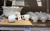 Wide angle of entire set showing punchbowl, thirteen cups, and ladle on cardboard surface with sunlight shadows.