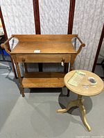 Full view of vintage wooden wash stand with drawer and small round side table next to it.