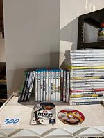 Two stacks of game cases on shelf with two loose discs on table: MVP Baseball 2005 and Mario Superstar Baseball