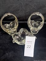 Three clear glass art pieces including two baskets and one bowl arranged on black background.