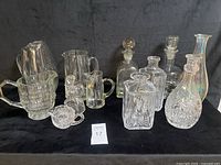 Wide view showing the entire lot of 12+ glass and crystal pitchers, decanters, and bottles on black background