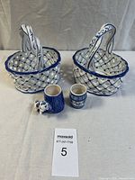 Two blue and white hand-painted ceramic baskets with lattice design and handles, displayed alongside three small blue and white ceramic items: a jug, a cylindrical container, and an animal figurine.