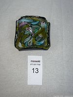 Top down view of colorful fused glass dish showing abstract design in green, blue, pink, white, yellow and silver foil accents with scalloped edges.
