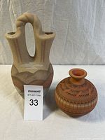 Photo of two pottery vases, one tall double-spouted wedding vase with earth tone textured matte finish and one smaller round terracotta vase with etched geometric and feather motifs.