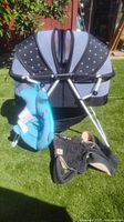 Photo of collapsible bassinet with canopy and frame, whale-shaped baby bath hanging, ErgoBaby carrier on grass