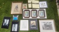 Nine framed art pieces and two boxed new frames displayed on grass, showing a variety of artwork styles and frame materials.