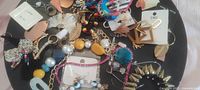 Top view of assorted eclectic jewelry pieces including earrings, bracelets, and necklaces in various colors and materials on a black surface.
