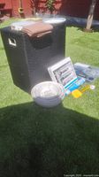 Photo of large black woven hamper, nested white mixing bowls, boxed silverware set, and packaged kitchen utensils on grass