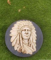 Front view of the circular resin wall plaque showing a detailed relief of an Indigenous American man with feather headdress in beige against a dark brown background
