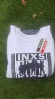 Folded white INXS Kick World Tour sweatshirt showing front black silhouette graphic with repeated 'KICK' text on sides and main logo center, with all access pass placed on top.