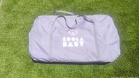 Gray fabric carry bag with handles, Koola Baby logo printed in white on the front, placed on green turf.