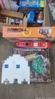 Photo showing boxed Mech 5 robot toy, Pac-Man ghost light made with blocks, green toy soldiers, red Nerf gun, and board game boxes with trading cards below.