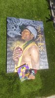 Large fantasy-themed canvas artwork showing man with cap and hand glowing near chest, with smoke and Asian script. Three smaller colorful fantasy canvas paintings displayed at bottom of large painting on grass.