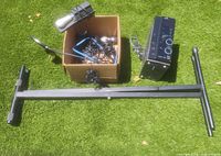 Wide view of lot laid out on grass showing keyboard stand, cardboard box with cables and microphones, keyboard foot pedals, and JVC media system.