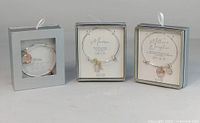 Front view of three charm bracelets in individual silver gift boxes with clear display fronts showing bracelets and engraved charms.