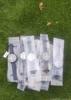 Five Oulm watches in unopened packaging displayed on grass. Two color varieties visible: black and navy blue straps.