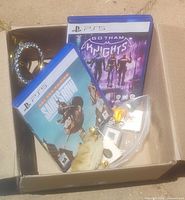 Overall view of two PS5 game cases, assorted pinback pins, a lucky rabbit foot, and small trinkets inside a cardboard box.