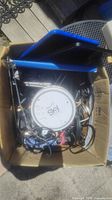 Box containing Sky Lite satellite dish, blue tablet, assorted AV connectors, charging cables, and small electronics.