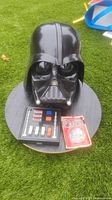 Photo showing Darth Vader helmet on a black surface with chest box and packaged Return of the Jedi pin beside it, highlighting the helmet's gloss and chest box controls