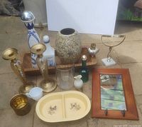 Photo of various vintage decorative home décor items including brass candlesticks, ceramic and glass vases, pitchers, decorative bottles, mirrors, an oil lamp, serving dish, and wooden bowl.