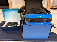Acer Windows Mixed Reality VR headset in blue and black, placed inside a blue box with the two VR controllers visible behind it.