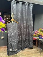 Photo showing three black drapes hanging outdoors, highlighting the grey embroidered cherry tree pattern and grommets.