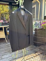 Full front view of black Calvin Klein men's tuxedo jacket hanging on a stand outside showing shape and condition.