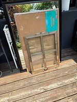 Photo showing large mirror with dark plastic frame behind window-style picture frame and large cork board placed on wooden deck
