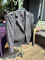 Grey wool kilt jacket and waistcoat displayed on a hanger outside, showing tailored design and button details on the jacket sleeves and shoulders.