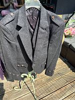 Photo of grey wool kilt jacket hanging on a hanger, showing the front with epaulets, button details, and inner lining.