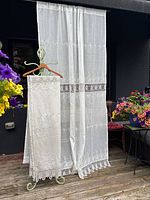 Full view of two ivory sheer lace curtain panels hanging outdoors showing intricate floral embroidery and lattice lace border.