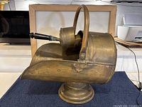 Side profile of antique brass coal skuttle showing curved shape and handle.