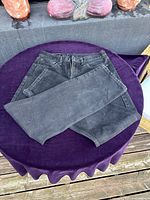 Front side view of black Levi's 505 jeans folded and laid on purple velvet fabric on a table outdoors.