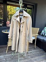 Front view of the khaki trench coat on a hanger showing collar, buttons, pockets, and belt detail