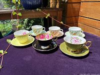 Front view of 6 vintage teacup and saucer sets in pastel colors with floral patterns and gold accents.