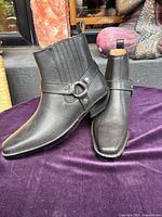 Front and side view of black leather ankle boots showing decorative ankle strap and elastic ribbed shaft panel.