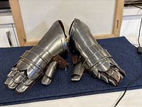 Pair of large medieval style metal gauntlets side by side showing front and top