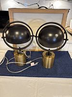 Pair of modern table lamps with brass cylindrical bases and black dome-shaped adjustable shades shown on a dark cloth.