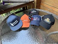 Front view of five caps laid side by side on a glass table with wooden background, showing logos and colors.