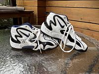 Pair of white Nike Air athletic shoes with black and navy detailing lying on a glass table showing side and profile view, signed on the side.
