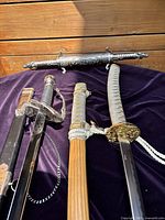 Top view showing basket-hilt sword with leather-textured scabbard, Japanese-style sword with wooden scabbard, and ornate double-ended metal scabbard.
