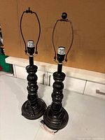 Close-up of a single black metal lamp base showing harp, gold accents, curved body, and cord