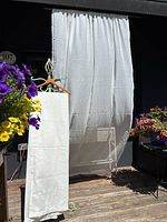 Set of sheer white/off-white curtain panels hanging outdoors, backlit showing fabric transparency and length